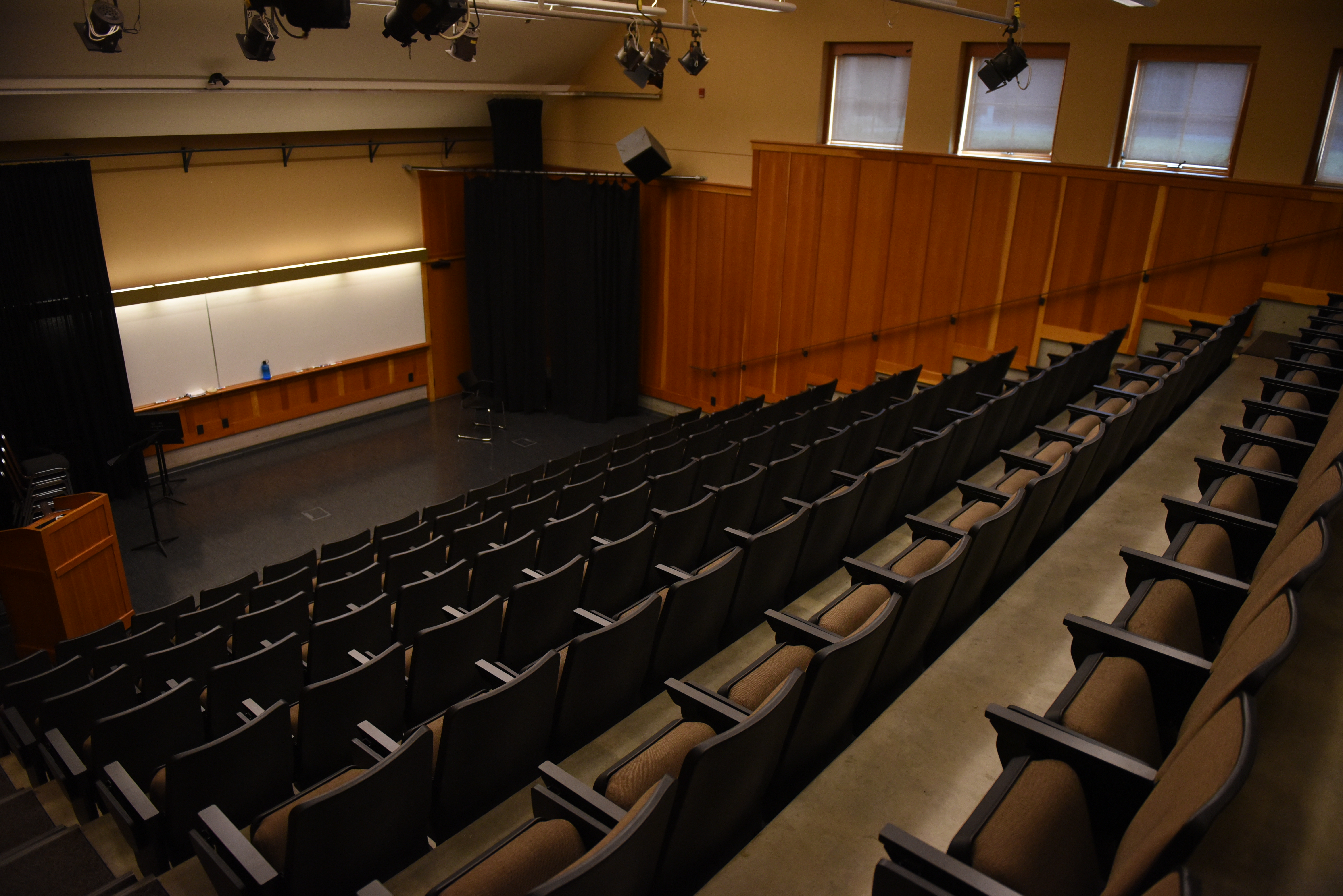 Indoor shot of lecture theatre, with empty chairs and a speaker area with white board.